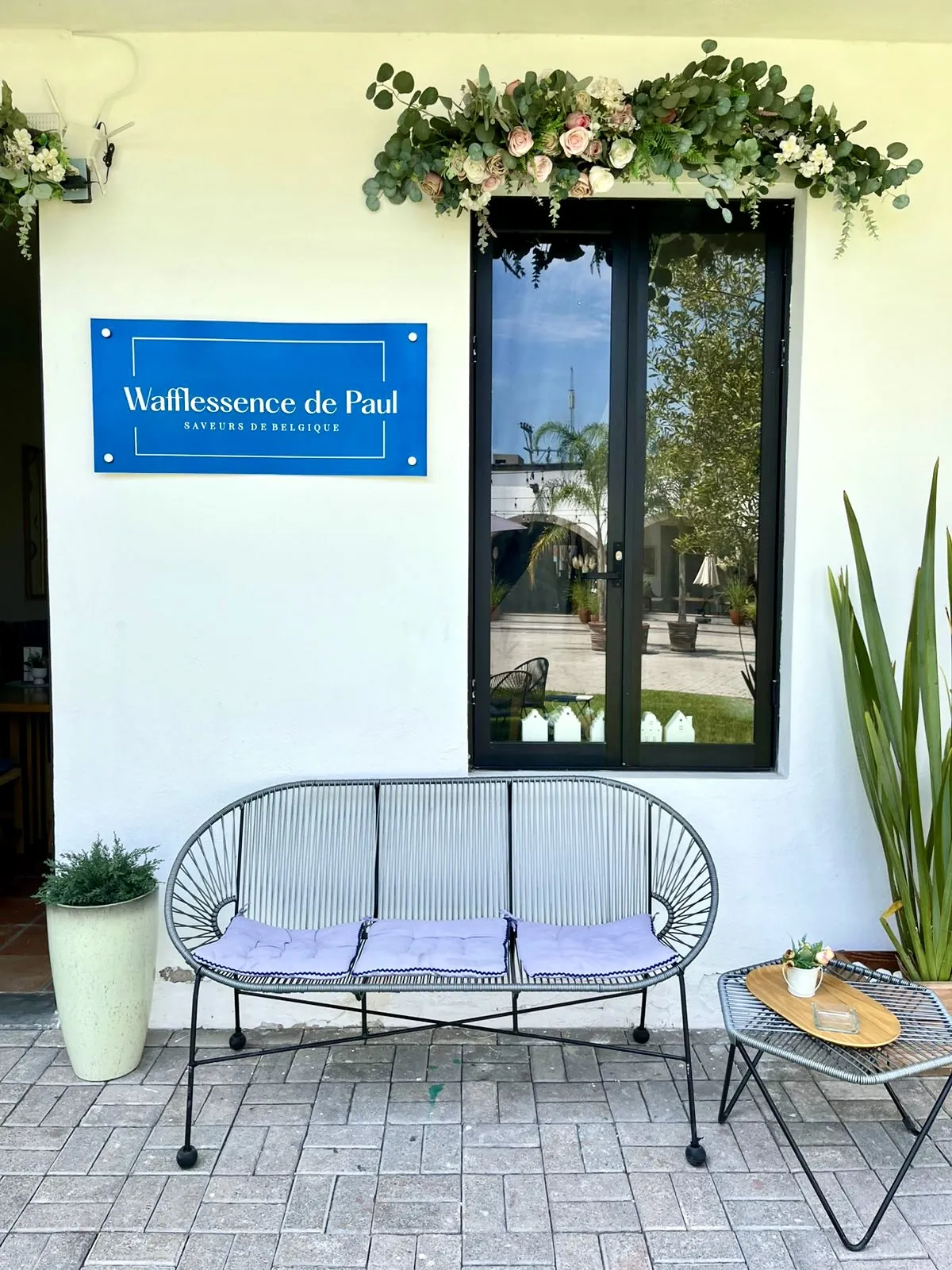 Banca frente a la fachada blanca con el logo y la ventana con flores
