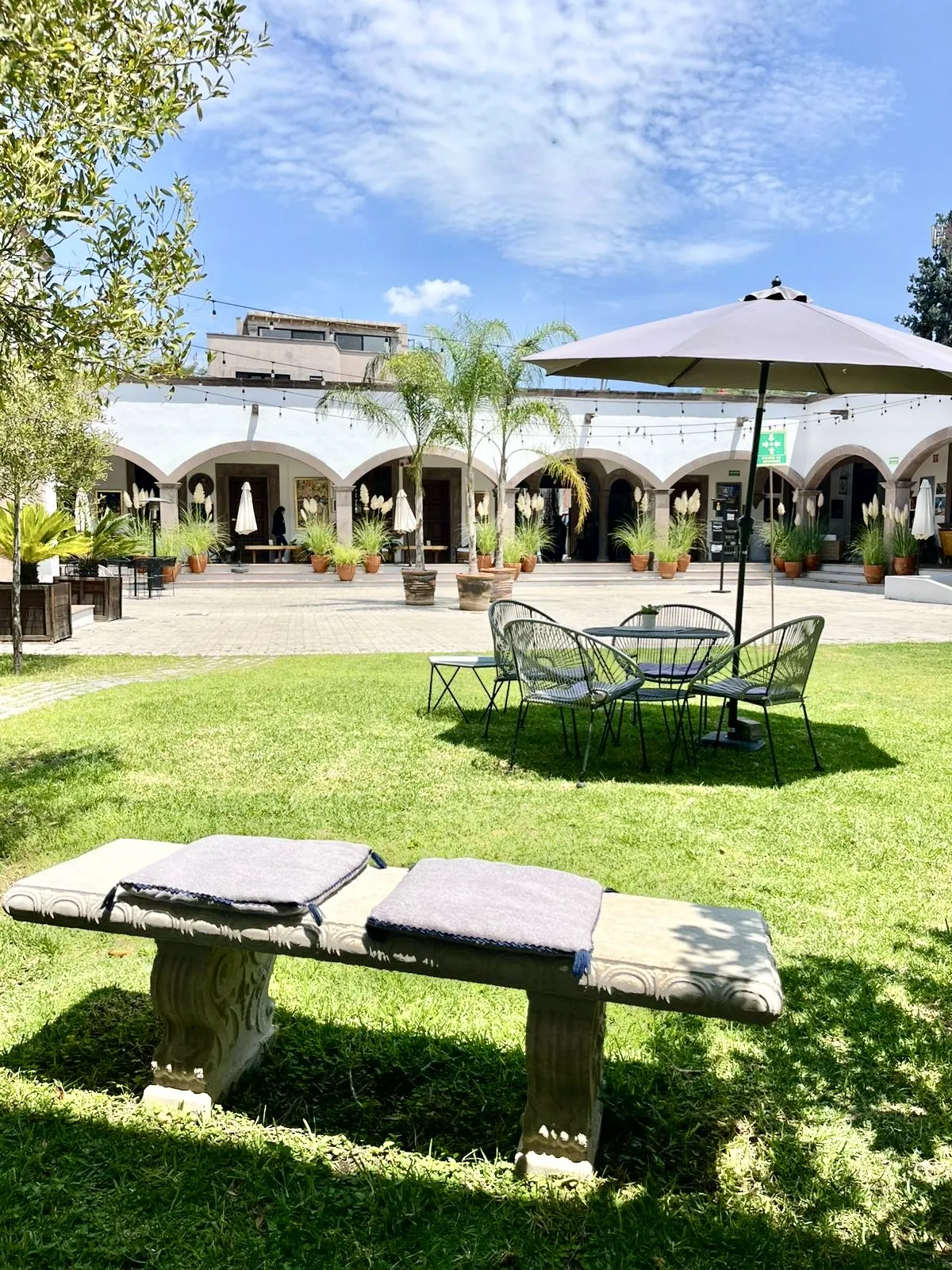 Patio con arcos, césped, palmeras y sombrilla