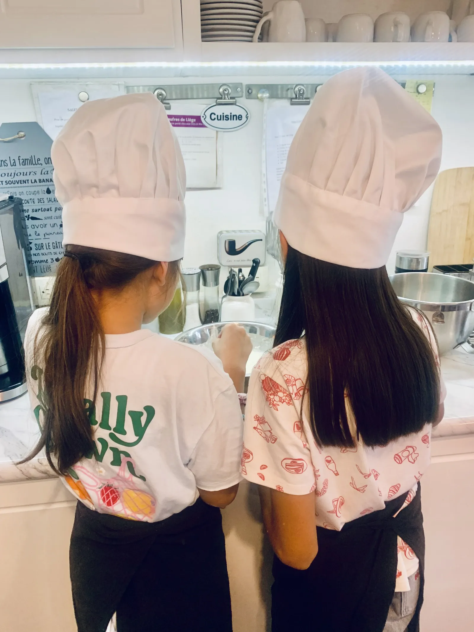 Dos niñas con gorros de chef, vistas de espaldas, en el taller